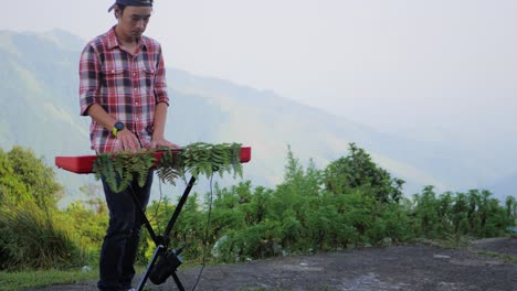 a stationary shot diagonally infront of a man, playing his electronic musical keyboard with a mountain view in the background