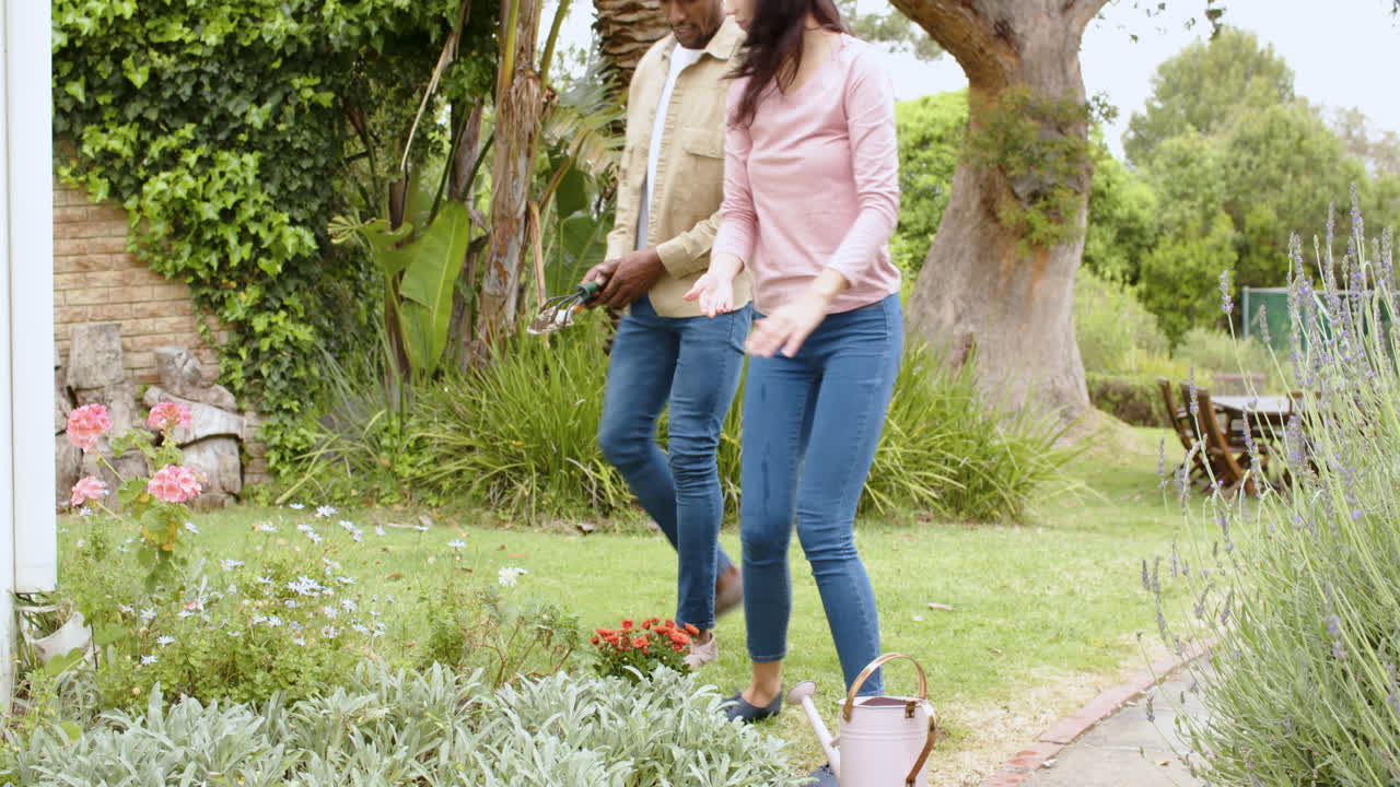 Diverse multiracial couple gardening together, enjoying nature and tending to plants outdoors