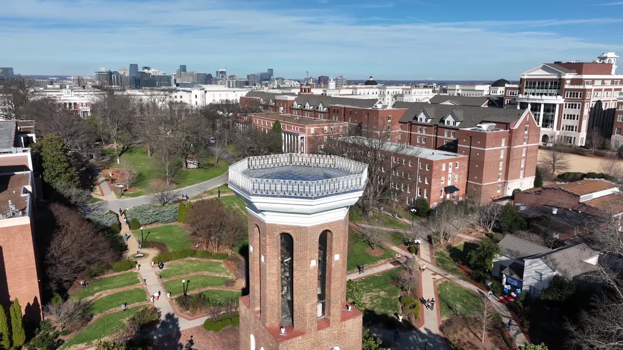 Belmont University in Nashville, mit ikonischem Glockenturm, akademischen Backsteingebäuden und Studenten, die über sonnendurchflutete Campuswege gehen. Sonniger Wintertag. Aufsteigende Weitwinkel-Luftaufnahme.