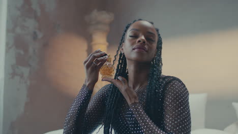 Cinematic-shot-of-a-dark-skinned-girl-showing-of-her-perfume-while-sitting-on-bed