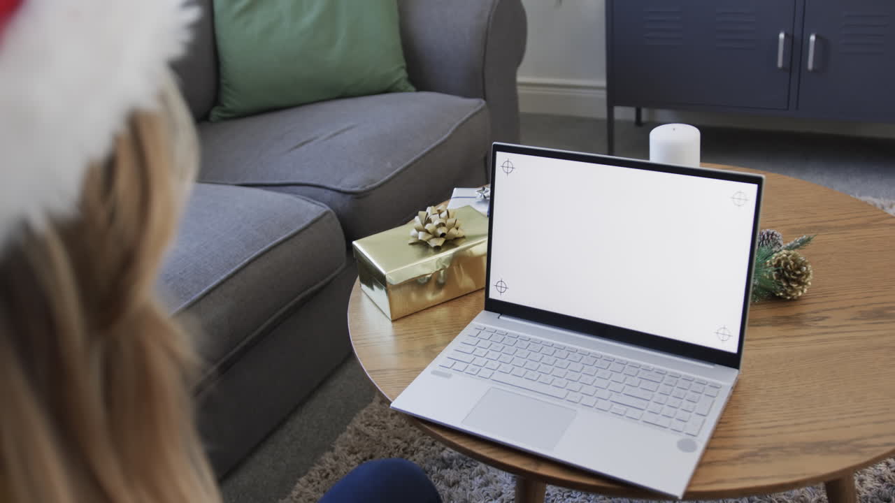 Donna di etnia mista felice che indossa un cappello di Babbo Natale e usa il laptop a Natale, con spazio per il testo, al rallentatore.