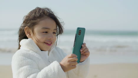 linda chica japonesa sosteniendo un teléfono inteligente en sus manos mientras pasa tiempo en la playa