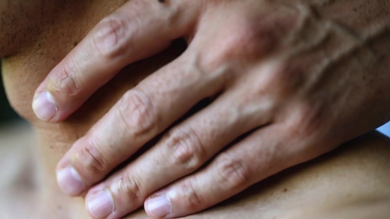 Massaggiare il collo e la spalla nudi di un uomo in una stanza illuminata, le dita della mano destra che massaggiano per alleviare la tensione.