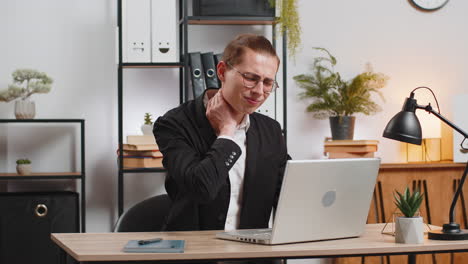 caucasian businessman guy sitting at desk working at laptop sitting at desk feeling pain in neck