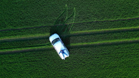 extreme life. guy laying on a moving white car in nature. young man travels on a car roof on green field background. top view.