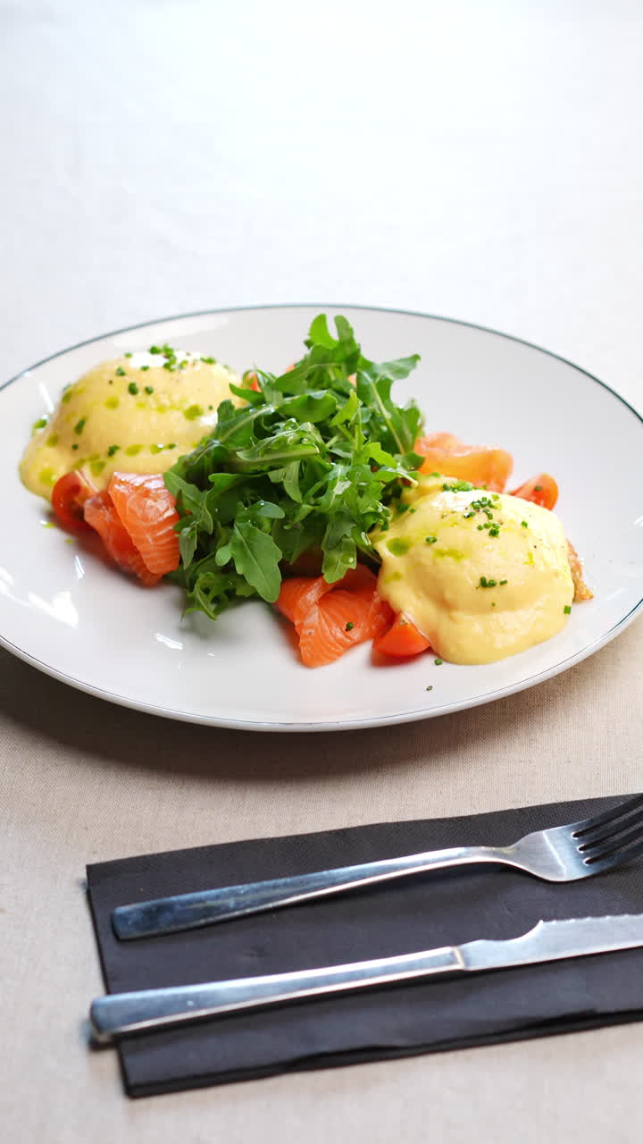 Eggs Benedict featuring poached eggs, hollandaise sauce, smoked salmon, fresh arugula, and chopped chives, served on a white plate, creating an appetizing culinary scene