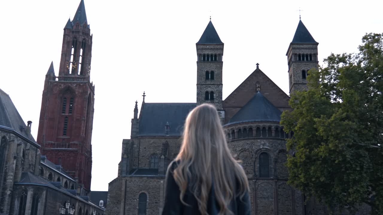 Woman on Vrijthof square in a sunny day, the historic center of Maastricht, Netherlands. The background is dominated by the iconic red tower of the Sint-Janskerk (St. John's Church)
