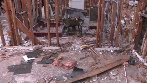 tilt up from a debris covered floor to a zoom in on a door and crumbling walls of a house in the process of being demolished