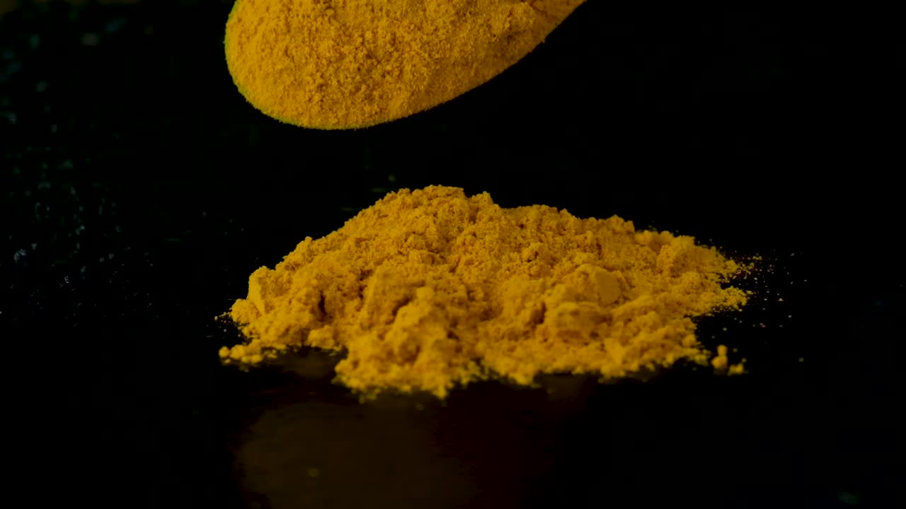Slow motion spicy yellow aromatic turmeric falling from wooden spoon onto pile isolated on black background, Studio shot