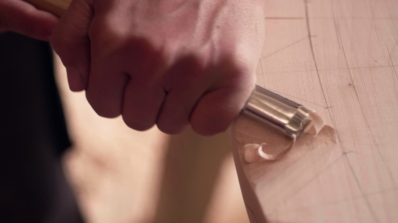 Female artisan's hand pushing a chisel through wood to create curly shavings during a woodworking process. Slow motion detailed view