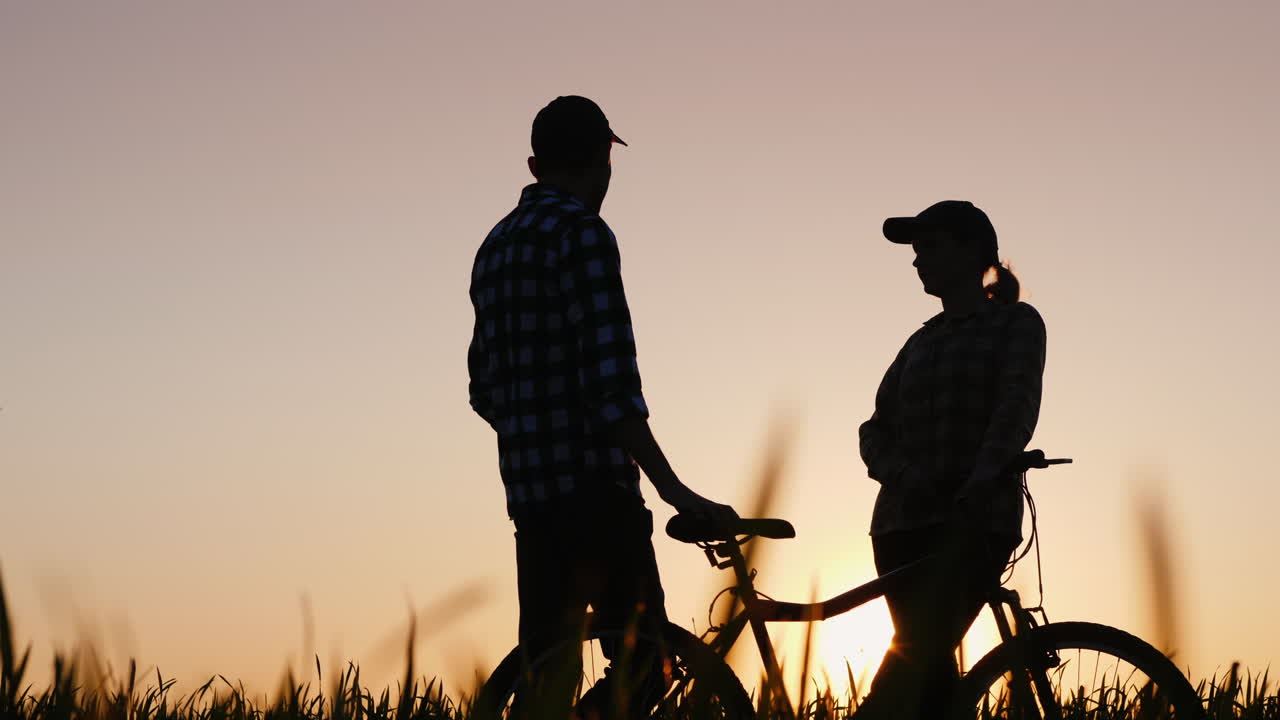 un hombre y una mujer disfrutan de un paseo nocturno al atardecer de pie con una bicicleta en la naturaleza
