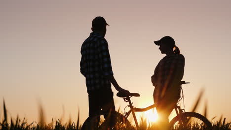un hombre y una mujer disfrutan de un paseo nocturno al atardecer de pie con una bicicleta en la naturaleza