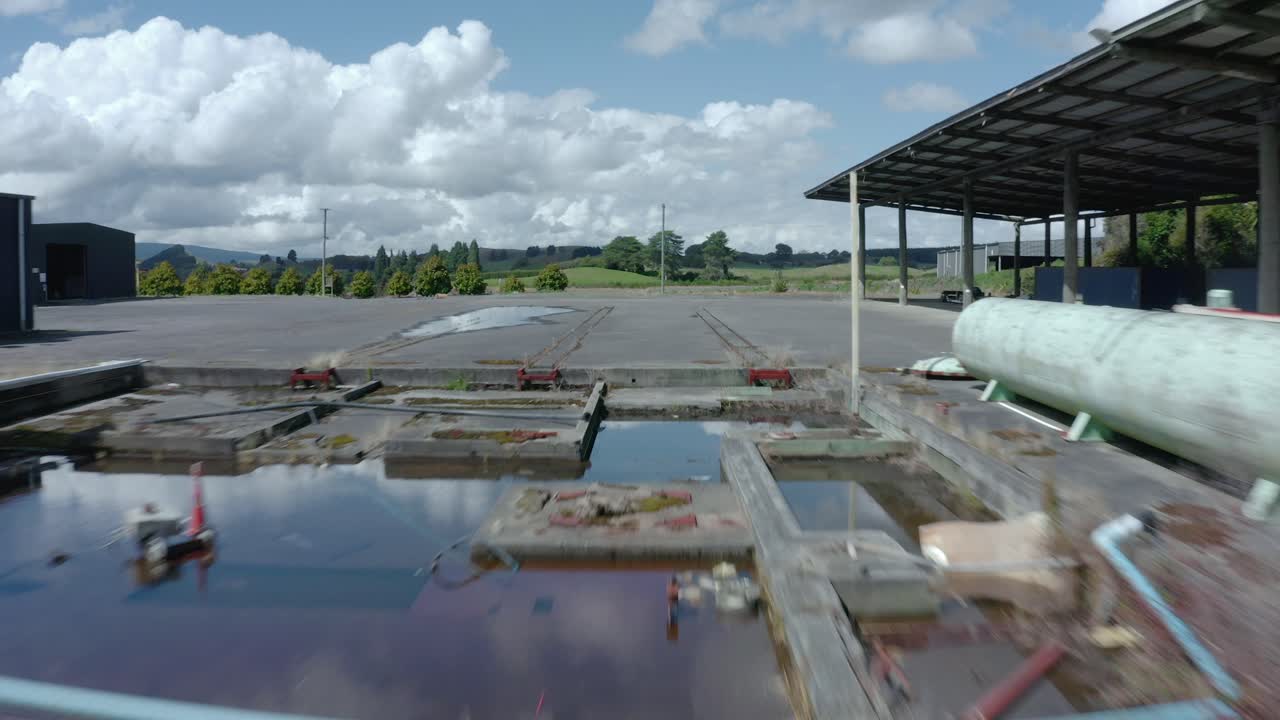 Antigo pátio ferroviário abandonado com fundações de construção cheias de água e um tanque.