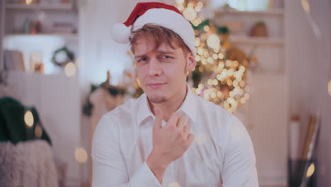 Confident-man-with-hand-on-chin-wearing-Santa-hat-at-home
