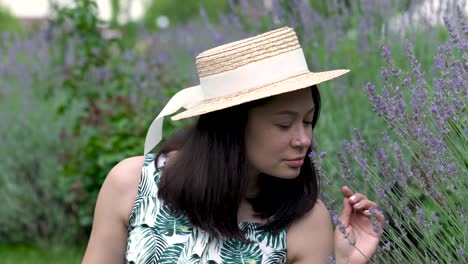 smiling asian girl in the hat smells lavender branch in the park. blurred lavender on the background.