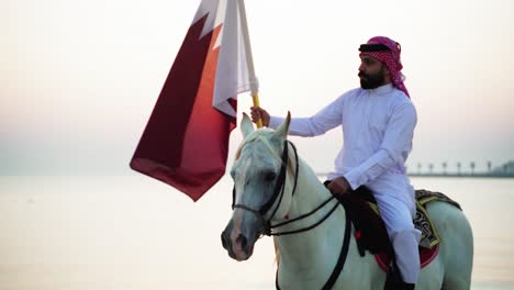 Un-Caballero-A-Caballo-Sosteniendo-La-Bandera-De-Qatar-Cerca-Del-Mar-6