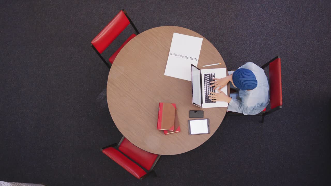 Asian female student wearing a blue hijab sitting and using a laptop