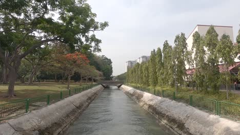 agua que corre a través del canal hecho por el hombre, con un parque a un lado y un restaurante al otro