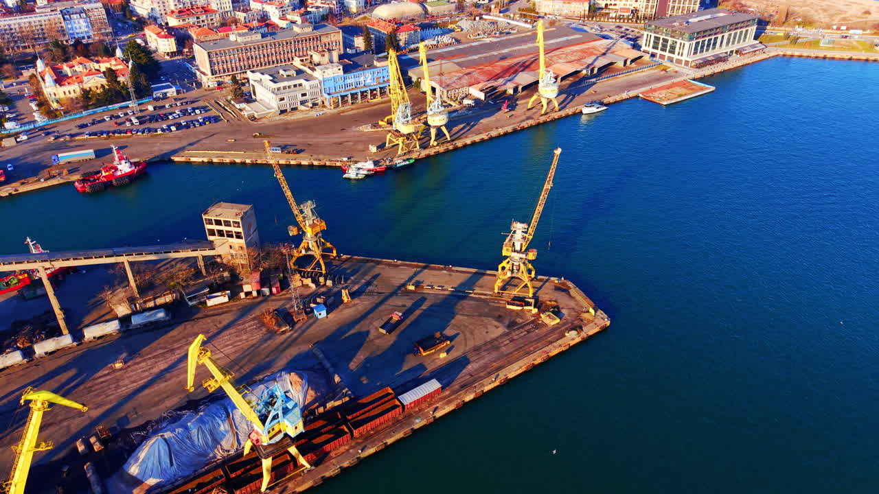 Widok z lotu ptaka na basen portowy z żółtymi dźwigami, czerwonymi holownikami i pobliskimi miejskimi budynkami administracyjnymi. Przemysłowe nabrzeże z dźwigami w porcie.