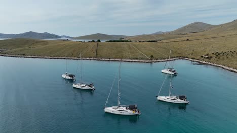anchored sailboats float on calm blue waters surrounded by rolling hills in kornati, croatia, drone ascend tilt down