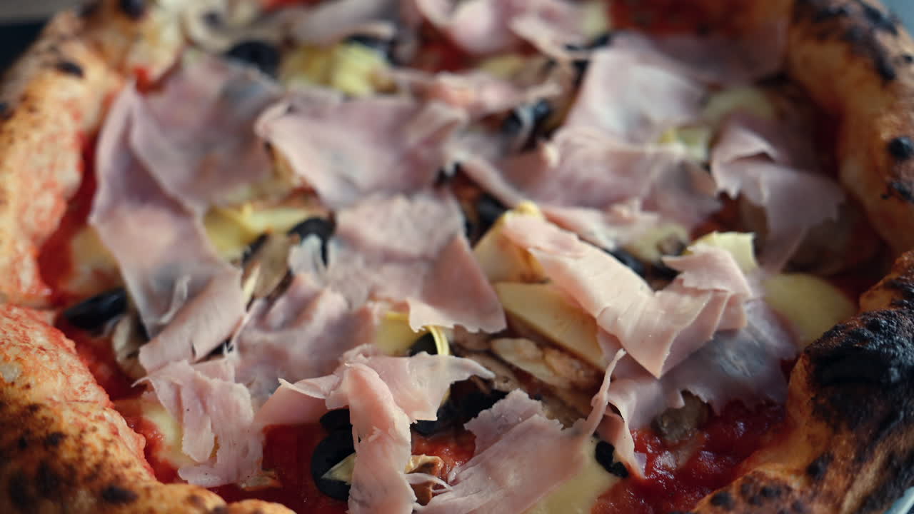 Primo piano di pizza appena sfornata condita con prosciutto, olive, funghi e formaggio