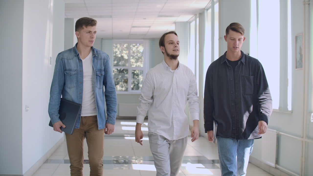 pasillos universitarios en la universidad. tres hombres van y ríen alegremente y hablan de la escuela y de la chica. instituto y comunicación diaria en la universidad juventud