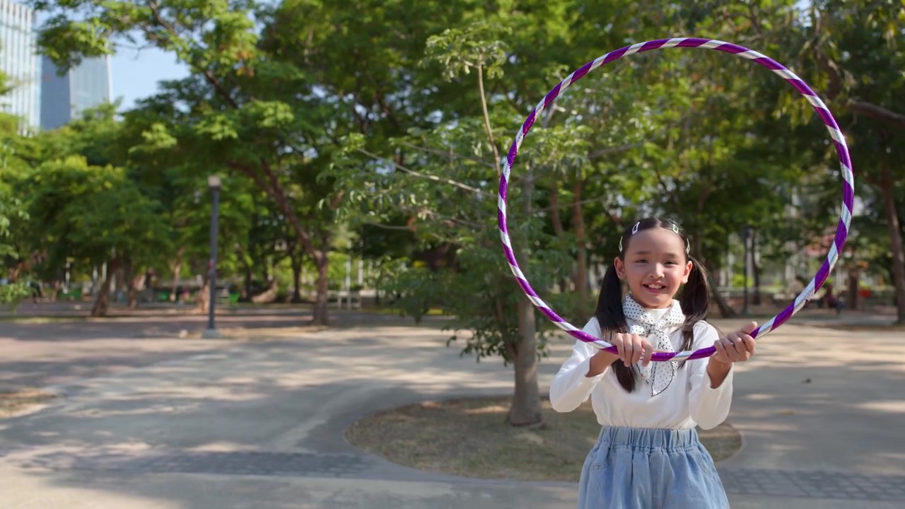 Güneşli bir parkta hula hoop ile oynayan genç kız.