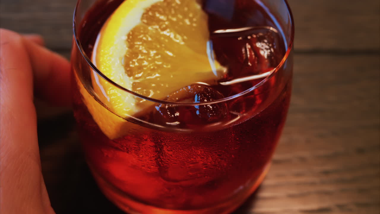 Tahta bir masanın üzerinde portakal dilimi ve buz küpleri olan bir Negroni kokteylinin yakın çekimi