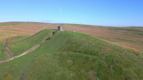 Stone-structure-on-hilltop-with-orbit-revealing-autumnal-colours-of-moorland-and-tall-radio-transmitters-on-hill-behind