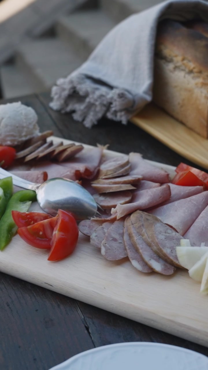 Video vertical de una tabla de embutidos rústica con carnes en rodajas, queso, verduras frescas y pan artesanal, perfecto para historias de redes sociales.