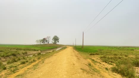 Filmmaterial,-Das-Die-Fahrt-Auf-Einer-Ländlichen-Unbefestigten-Straße-Durch-Trockenes-Marschland-Festhält,-Mit-Stromleitungen,-Die-Sich-Bis-In-Die-Ferne-Erstrecken