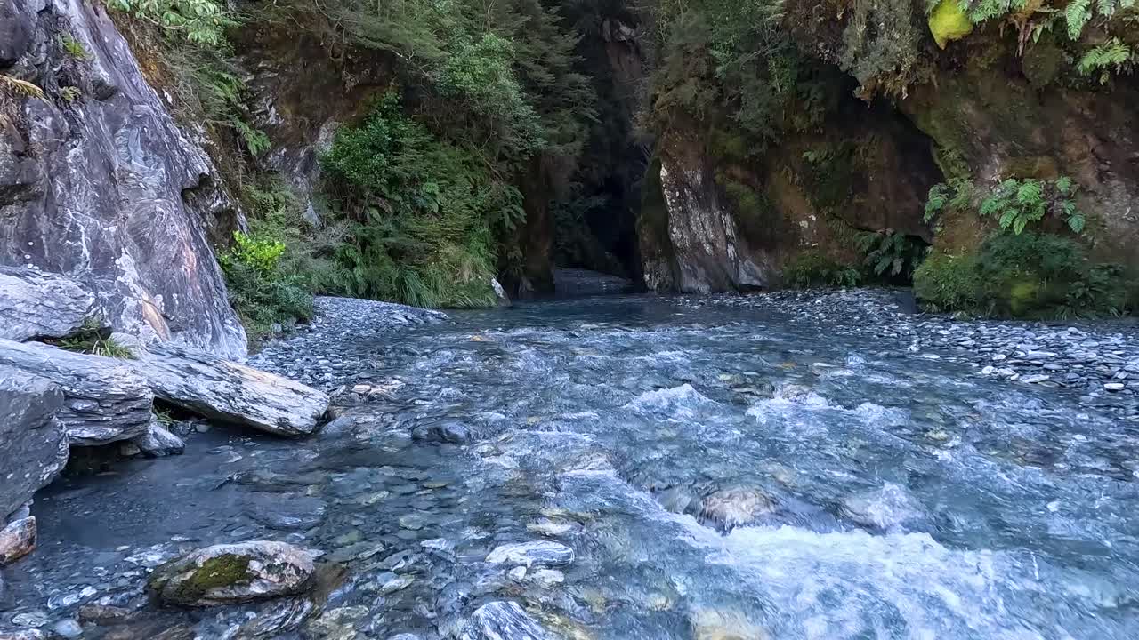 A view of Wilsons Creek Chasm from the outside along Haast Pass in New Zealand. You can see the small stream rushing out of the cave-like crack in the mountain