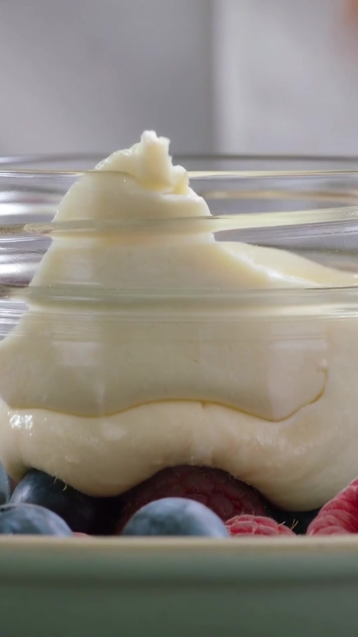 Vertical video: Lowering hands placing jar over fruit on counter spooning cream adding mint to eat