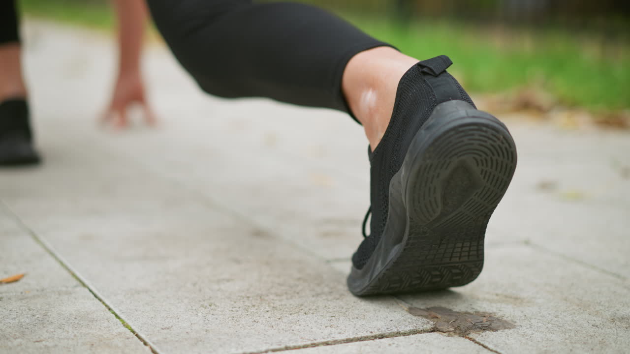 Close-up view of athlete's leg in sneakers on ground, blurred hand in background, preparing to take off for sprint, focus on footwear, athletic readiness, exercise motivation, outdoor training