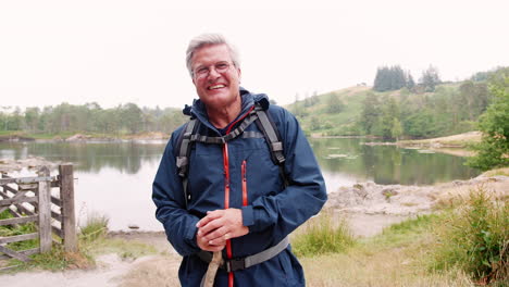 happy middle aged caucasian man standing near the shore of a lake holding a stick, close up, lake district, uk