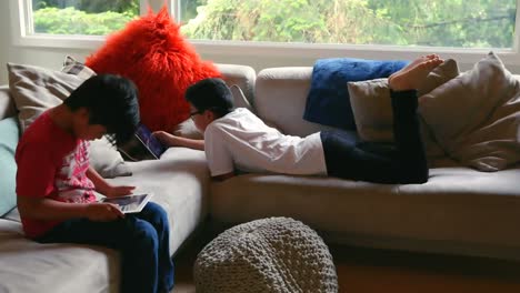 Animation-of-profile-icons-connecting-with-lines-over-asian-brothers-using-digital-tablets-on-sofa