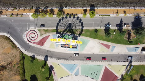 vista aérea de la rueda de la fortuna con sombra en el parque de atracciones de seixal, portugal, con coches que pasan por la calle durante el día