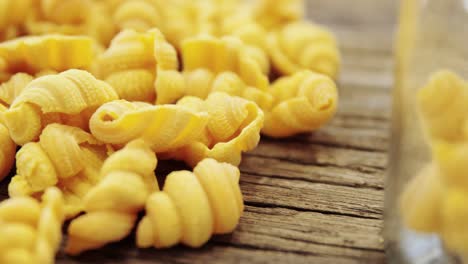 heap of pasta on wooden table and in one glass jar