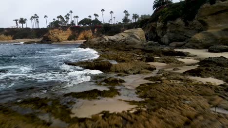 Volando-Bajo-Sobre-Rocas-Mientras-Aumenta-La-Altitud-En-Laguna-Beach,-Ca