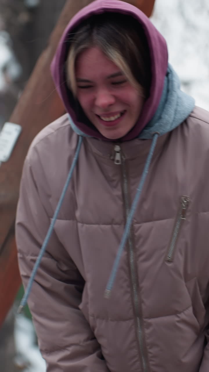 dama en traje de invierno sintiendo dolor en la rodilla mientras se inclina con árboles y fondo nevado, mostrando expresión de incomodidad, usando capucha y chaqueta hinchada, escena de invierno