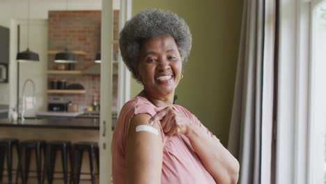 happy african american senior woman showing plaster on arm after covid vaccination