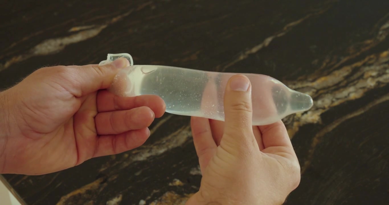 Persona che testa un preservativo riempito d'acqua, mostrando la durabilità, il controllo di sicurezza e il concetto di protezione contraccettiva