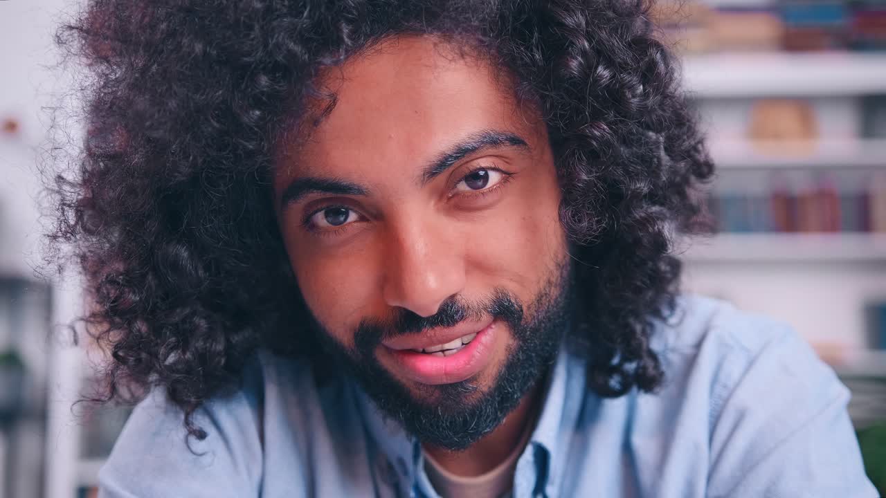 Homem bonito do Médio Oriente sorrindo encantadoramente sentado à secretária na sala de estar.