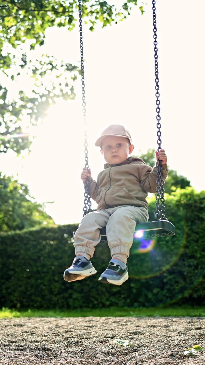Cheerful little boy swings on a swing on a playground in the park. 2 year old boy sits on a swing and laughs. Child plays on a playground. Child's walk in the fresh air