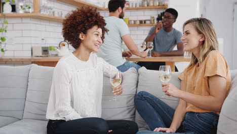 two couples relaxing on sofa at home with glass of wine talking together