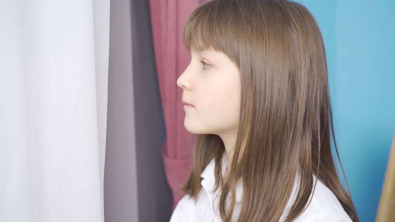 una niña deprimida y pensativa mirando por la ventana.