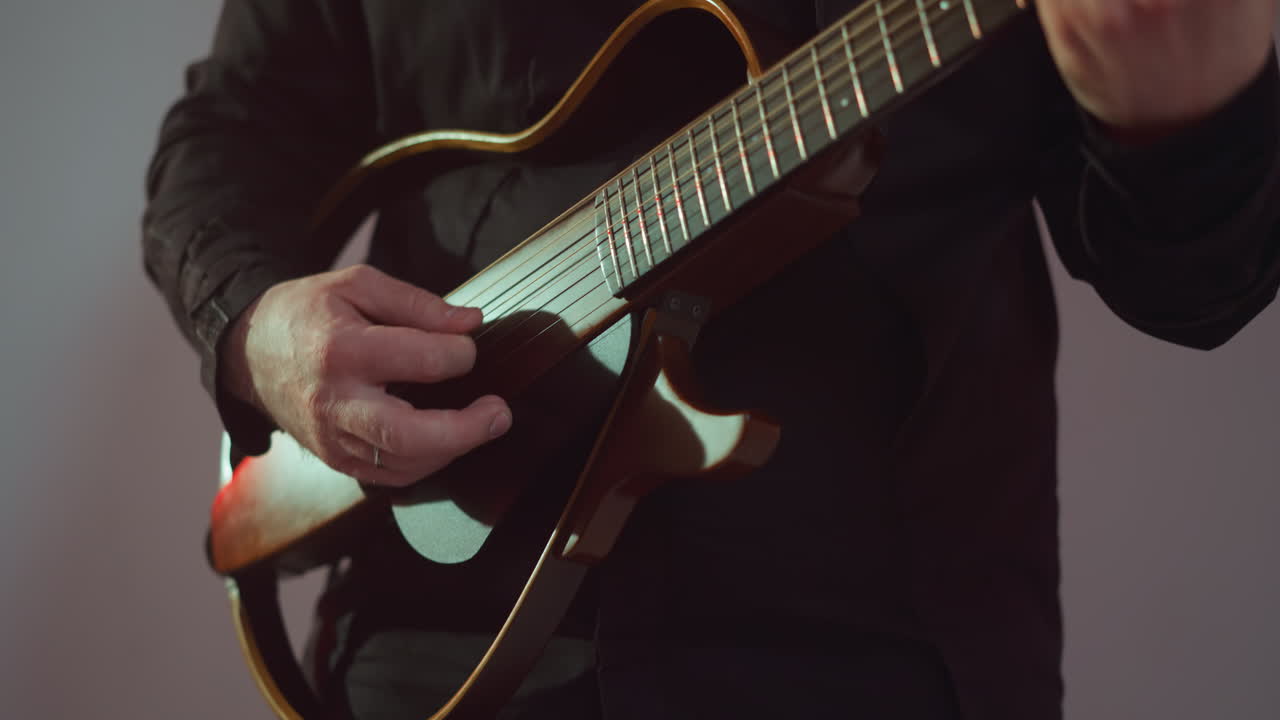 Faceless guitarist dressed in black, intently playing a red guitar, with a focus on hands and strings in a subtly lit setting. Ideal for musical performance and guitarist technique content