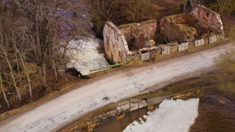 Abandoned-building-and-man-made-dam-with-powerful-river-stream,-aerial-view