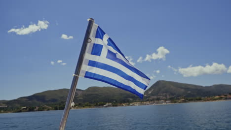 greek national flag blowing in the wind with sea and coast in background