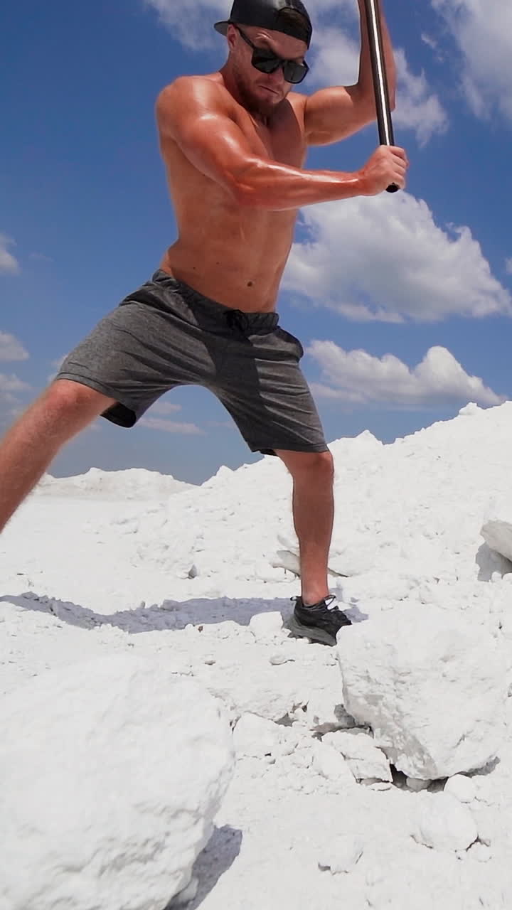 Muscular sportsman working in nature. Strong man with metal hammer breaking white rock on the mountain. Vertical video